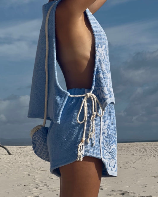 Person wearing a blue towel with a rope around their neck on a beach.