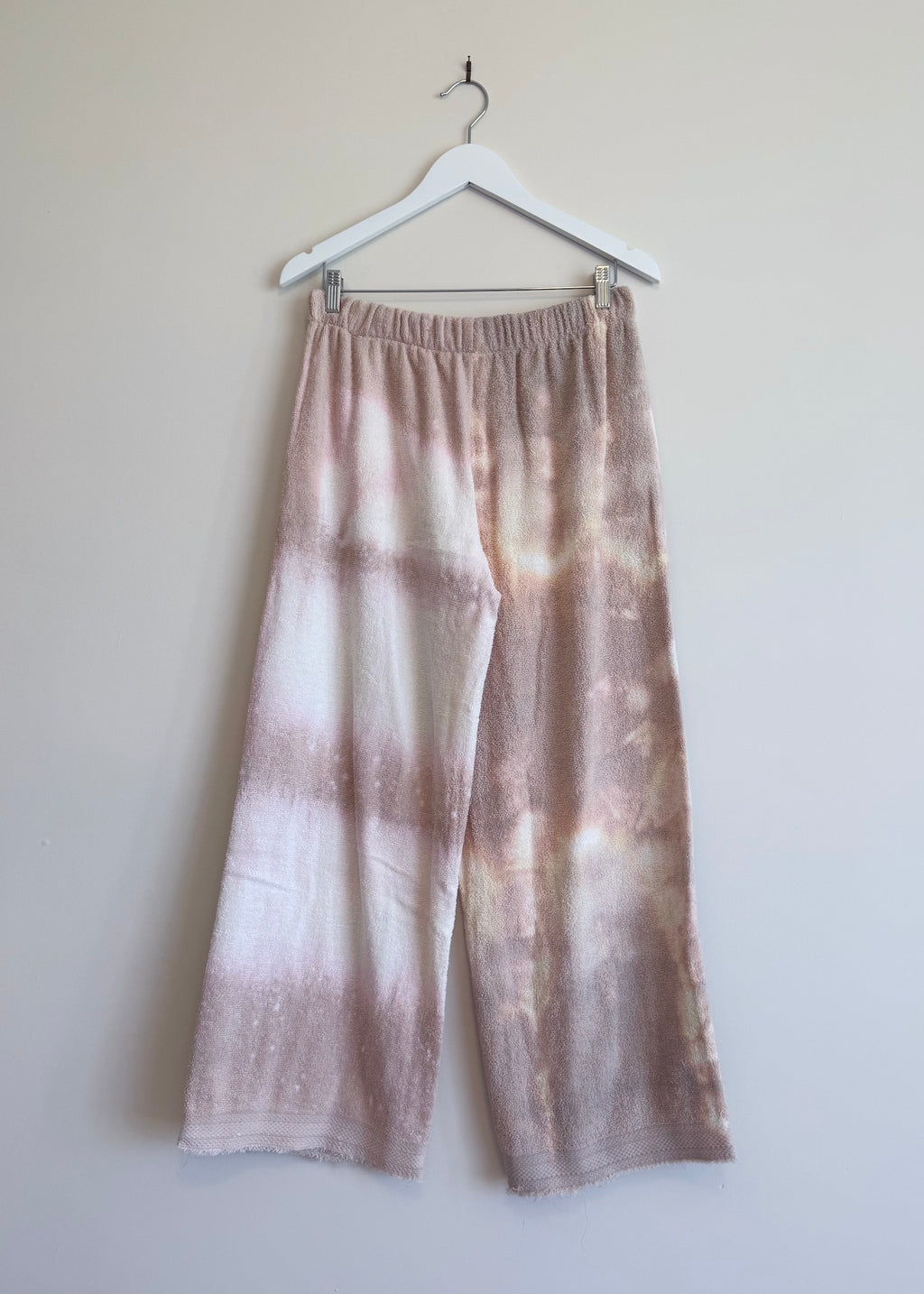 Tie-dye pants on a hanger against a plain background