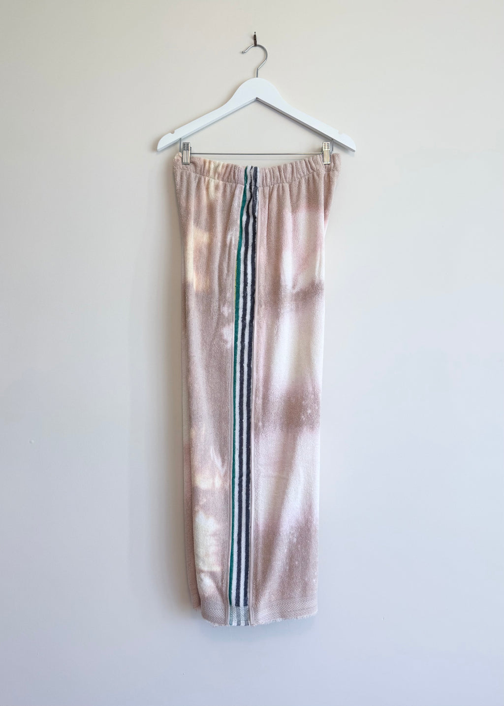Tie-dye sweatpants with three stripes hanging on a white hanger against a light background