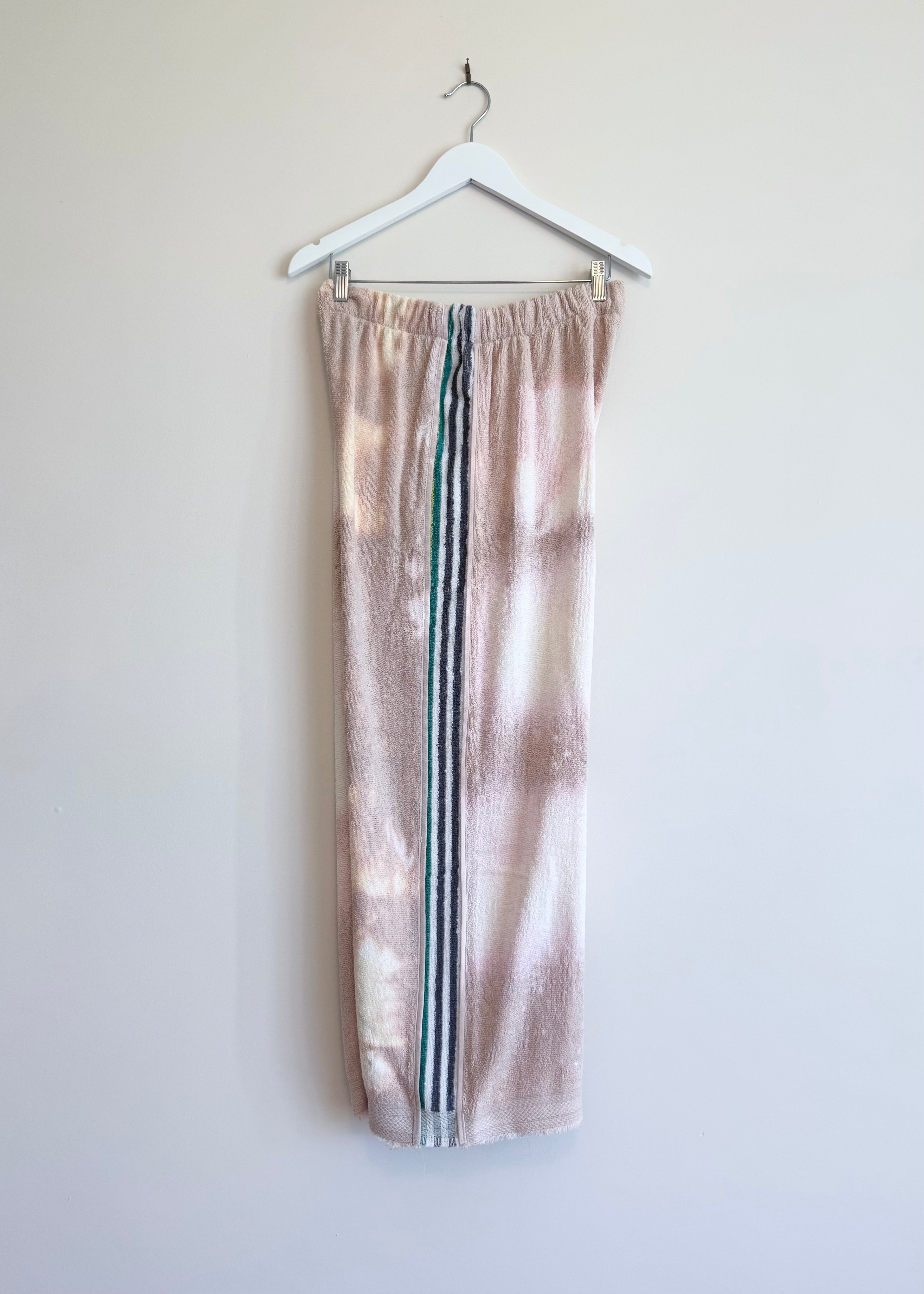 Tie-dye sweatpants with three stripes hanging on a white hanger against a light background