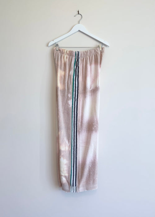 Tie-dye sweatpants with three stripes hanging on a white hanger against a light background