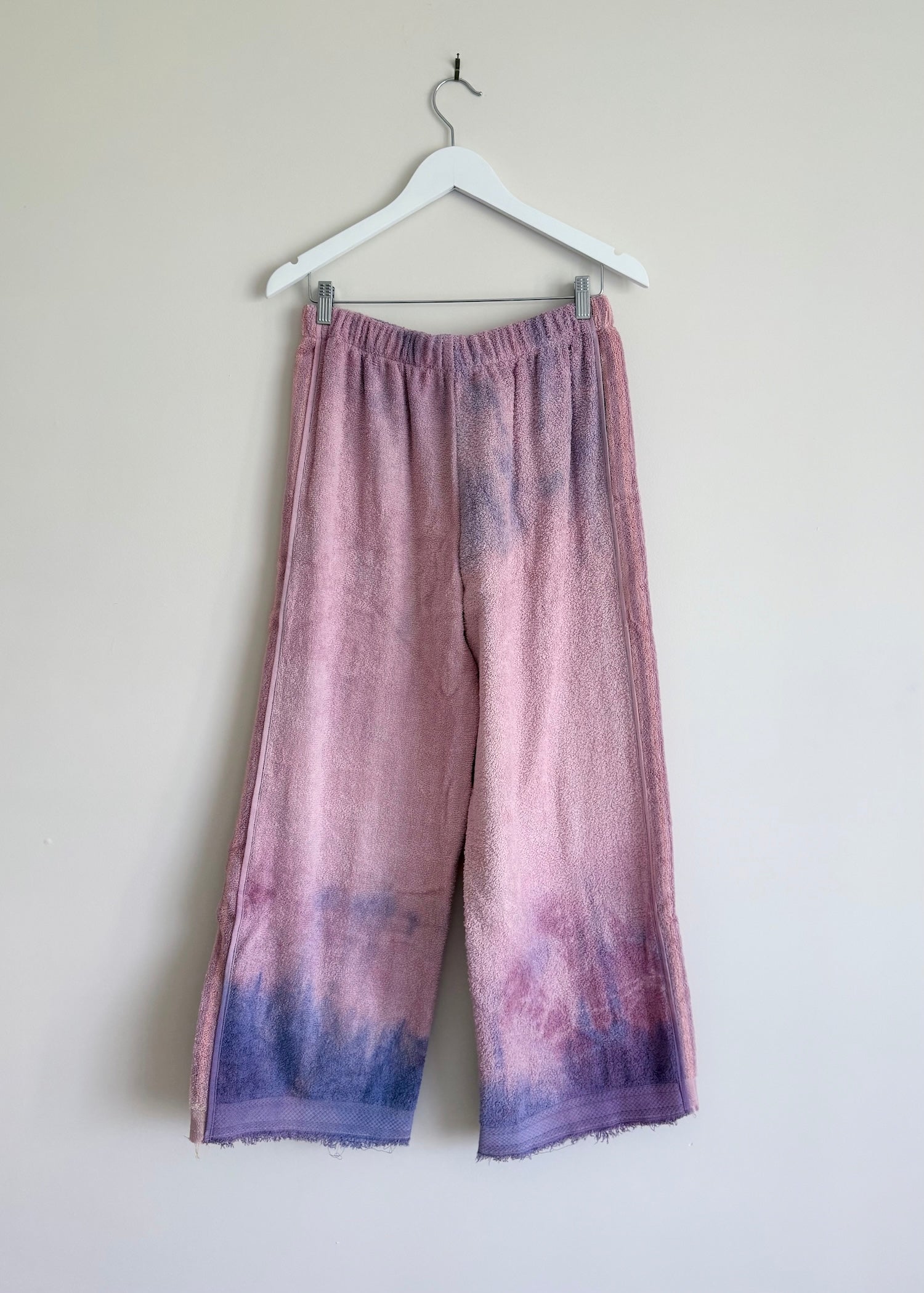 Purple tie-dye pants hanging on a white hanger against a plain background
