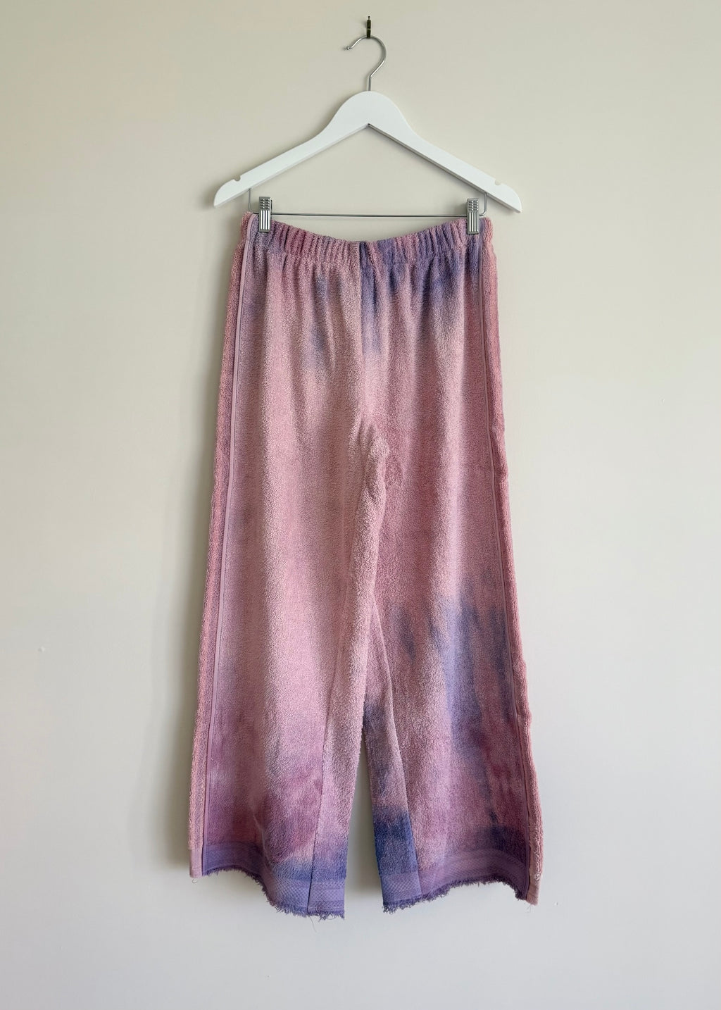 Purple and pink gradient pants on a hanger against a plain background