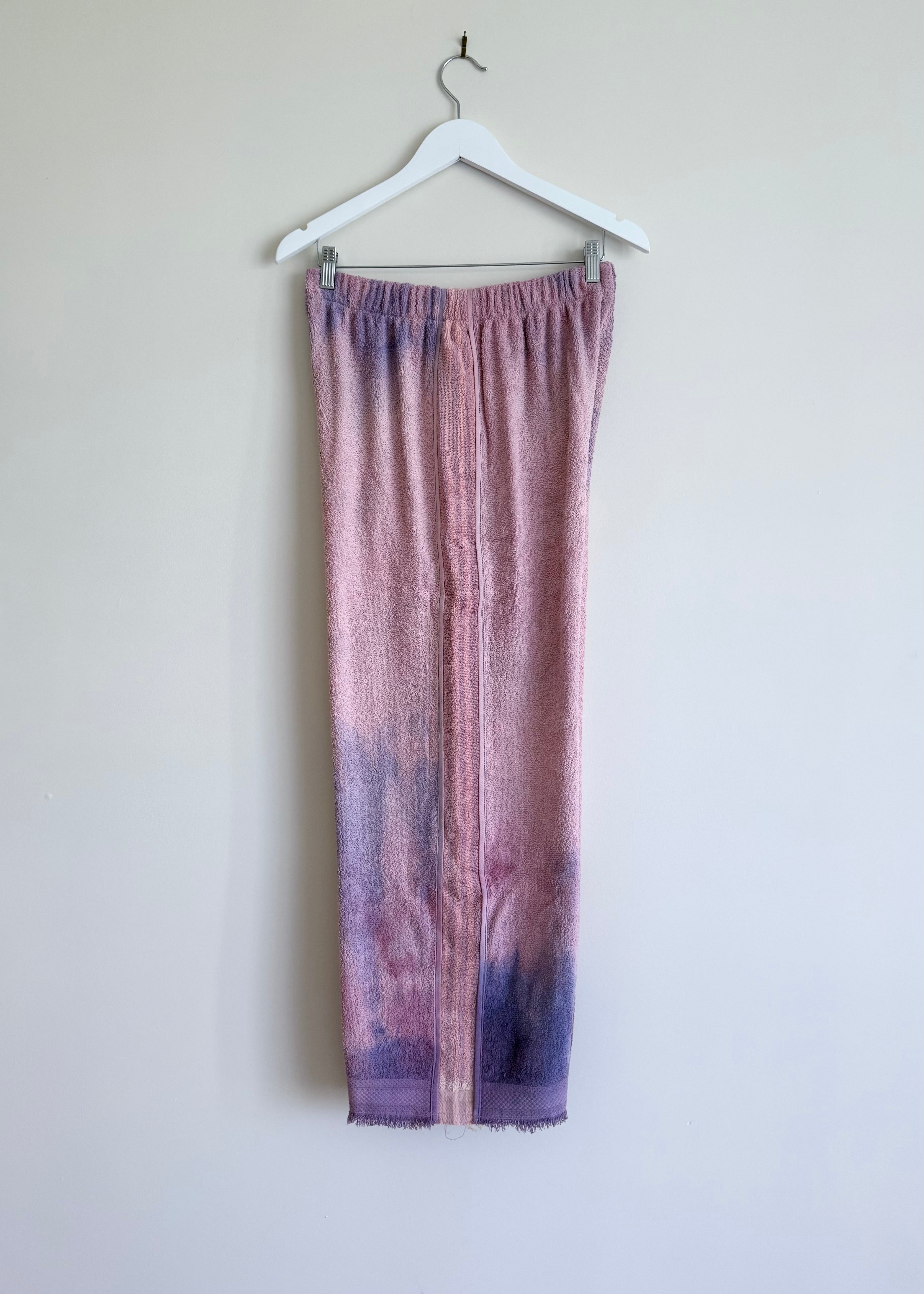Purple tie-dye pants on a hanger against a white wall