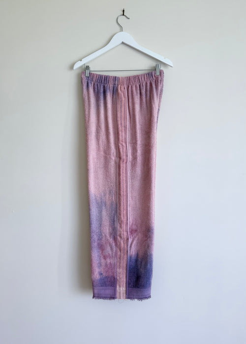 Purple tie-dye pants on a hanger against a white wall