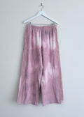 Tie-dye pants hanging on a white hanger against a light gray background