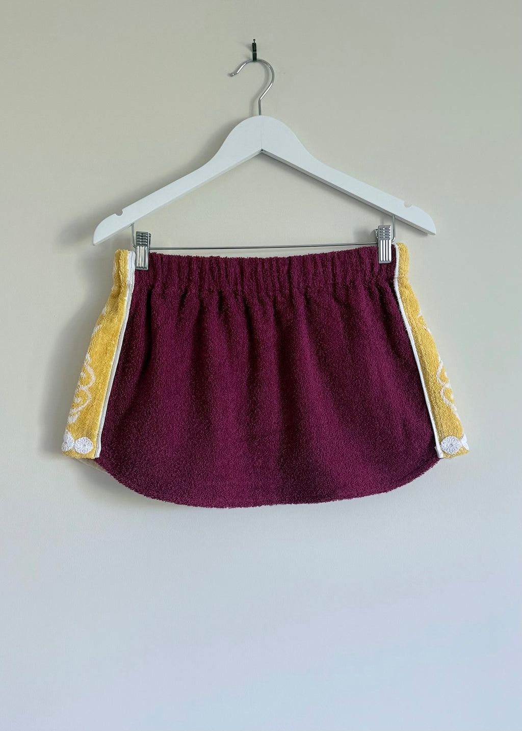Maroon shorts with yellow trim on a hanger against a plain background