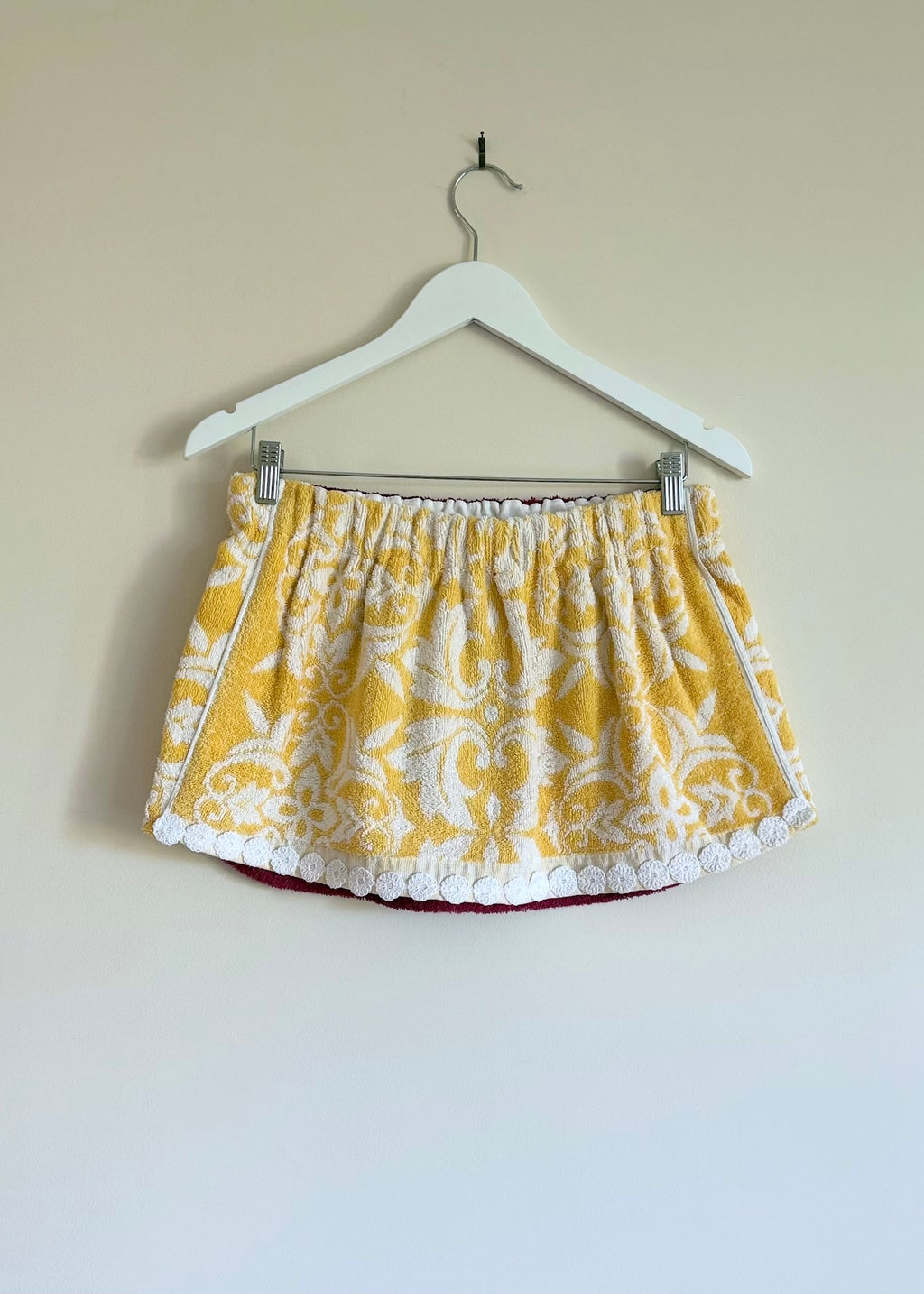 Yellow patterned skirt on a hanger against a beige wall