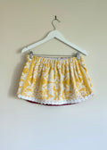 Yellow patterned skirt on a hanger against a beige wall